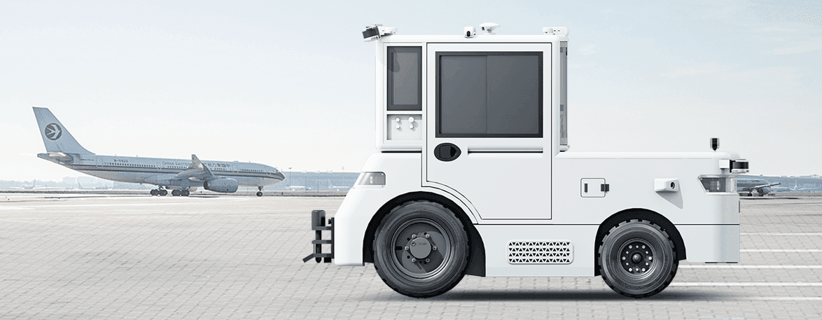 Autonomous white airport tug on a tarmac with a commercial airplane in the background.