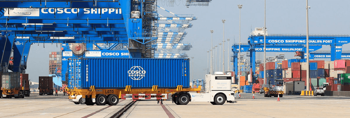 Automated truck transporting a blue COSCO SHIPPING container past large gantry cranes at Khalifa Port.